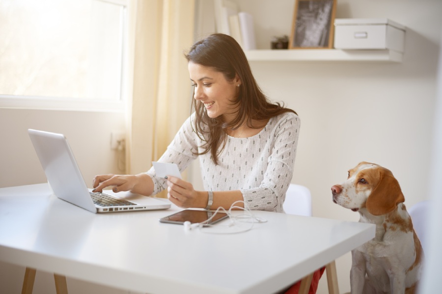 A young businesswoman using her credit card online with a dog sitting next to her.