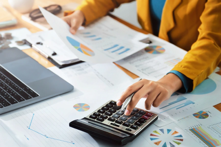 A woman accountant using a calculator and computer and holding a pen between their fingers.