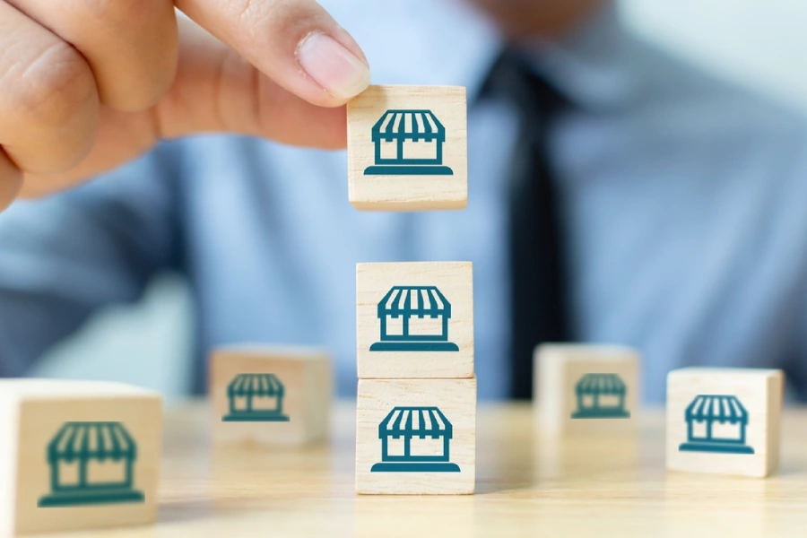 A person putting a wooden block on top of other blocks with a franchise store icon