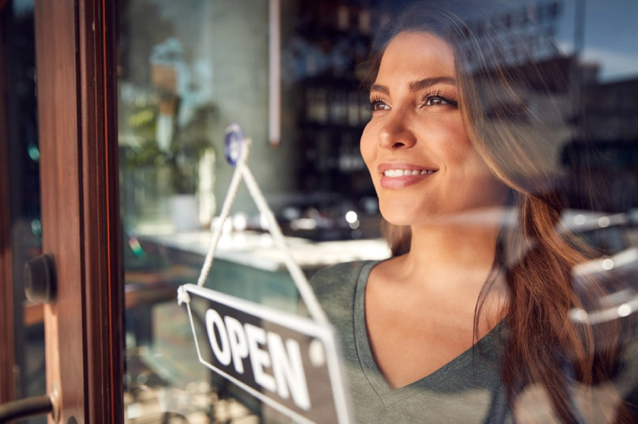 Female business owner smiling as she looks out of her store’s window.